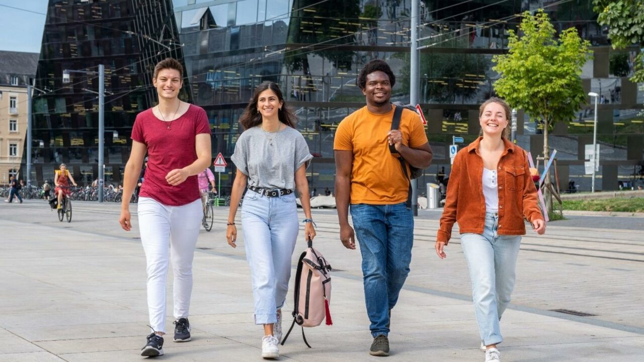 Vier Studierende im Gehen vor der Fassade der Universitätsbibliothek